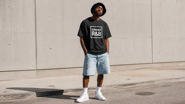 Confident model wearing a vintage-inspired R&B graphic T-shirt with denim shorts on a sunny city sidewalk